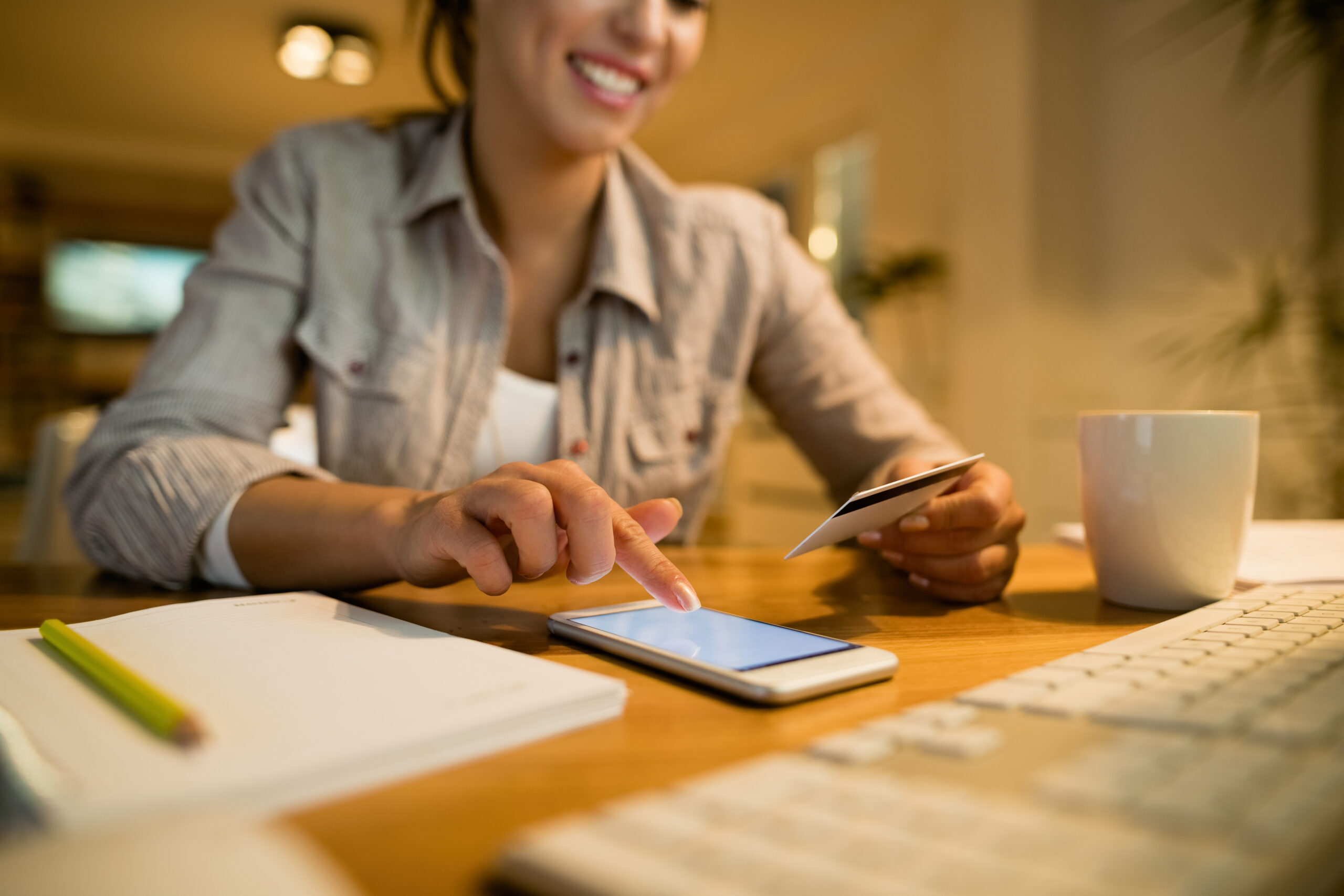 Close-up of woman sing credit card and smart phone while shopping online at night at home.